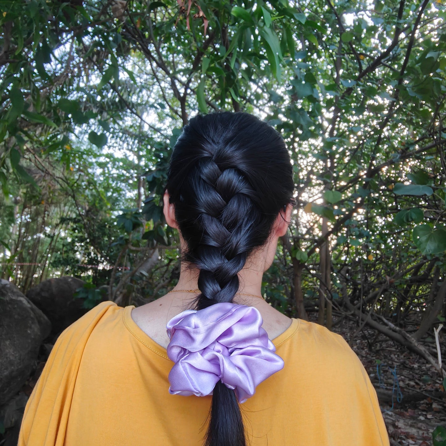 A girl tying the end of her braid with Amirah, the lavender satin scrunchie